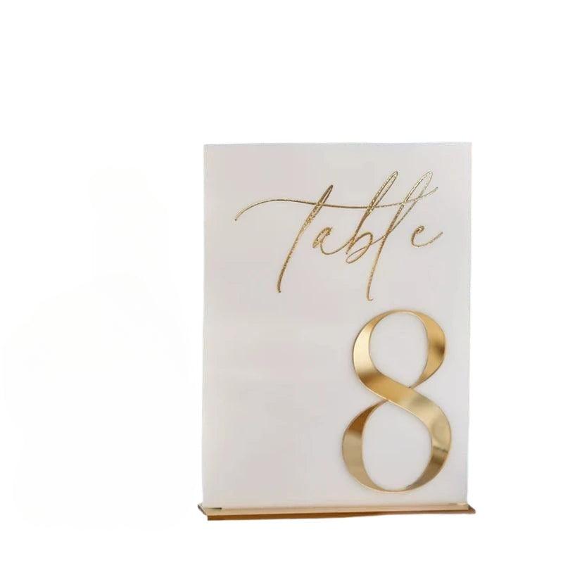 A white acrylic table number sign with the word 'table' written in cursive and the number 8 in gold mirror finish, mounted on a stand.